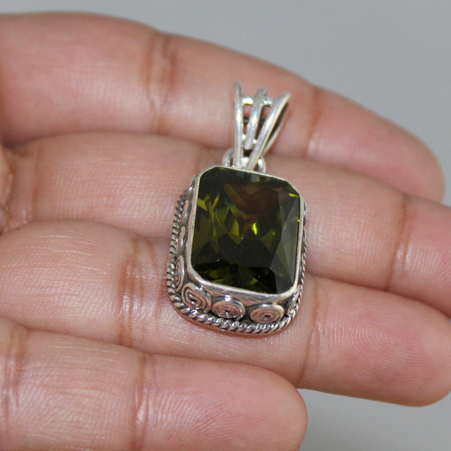 Silver pendant with a green gemstone held in a hand against a neutral background