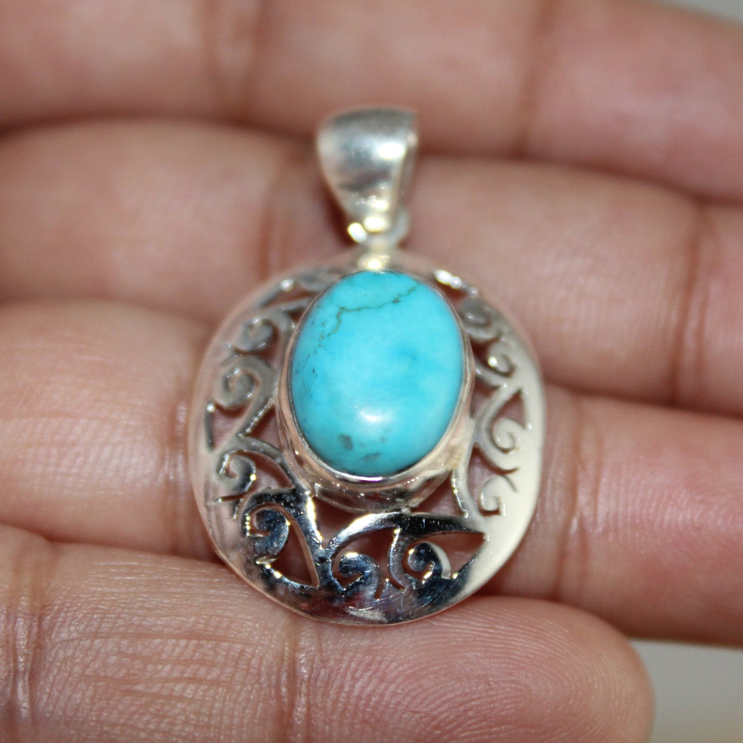Silver pendant with turquoise stone held between fingers