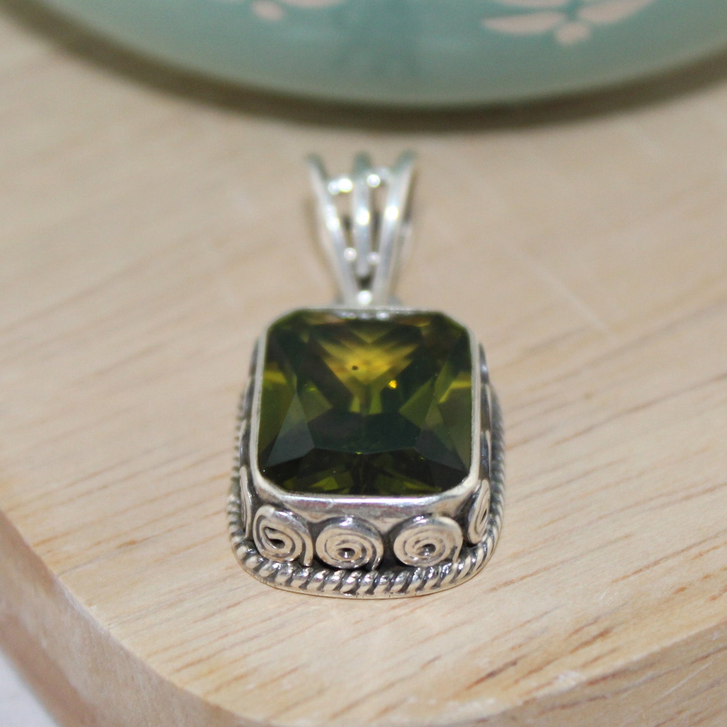 Silver pendant with a green gemstone on a wooden surface