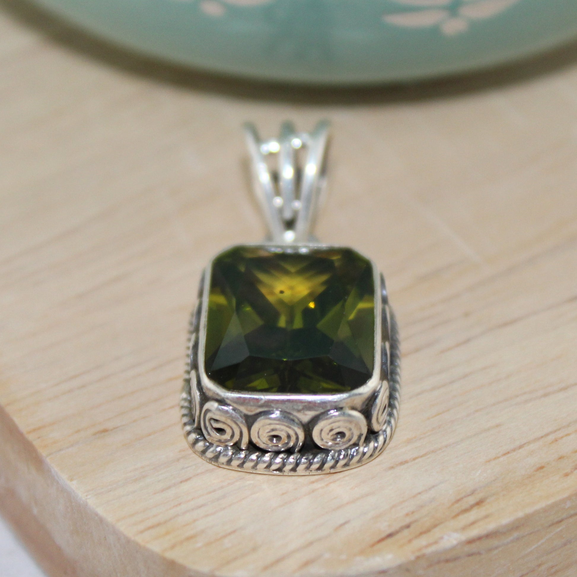 Silver pendant with a green gemstone on a wooden surface