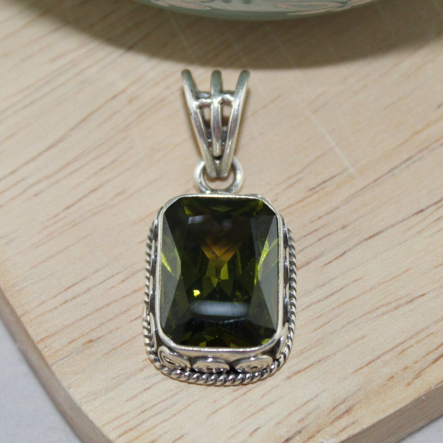 Silver pendant with a green gemstone on a wooden surface