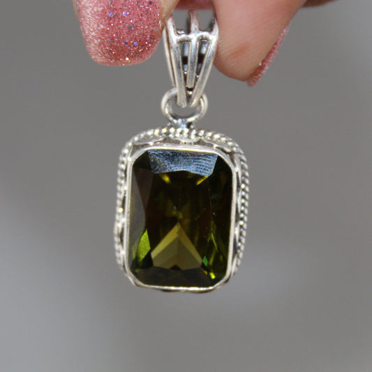 Silver pendant with a green gemstone held by a hand against a gray background