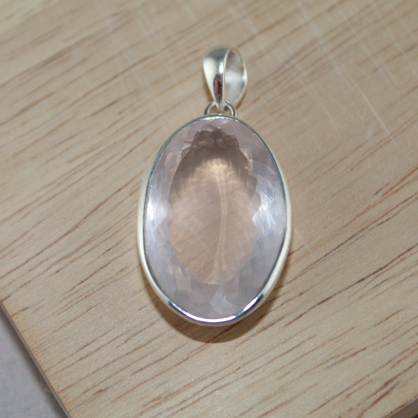 Silver pendant with a rose quartz stone on a wooden surface
