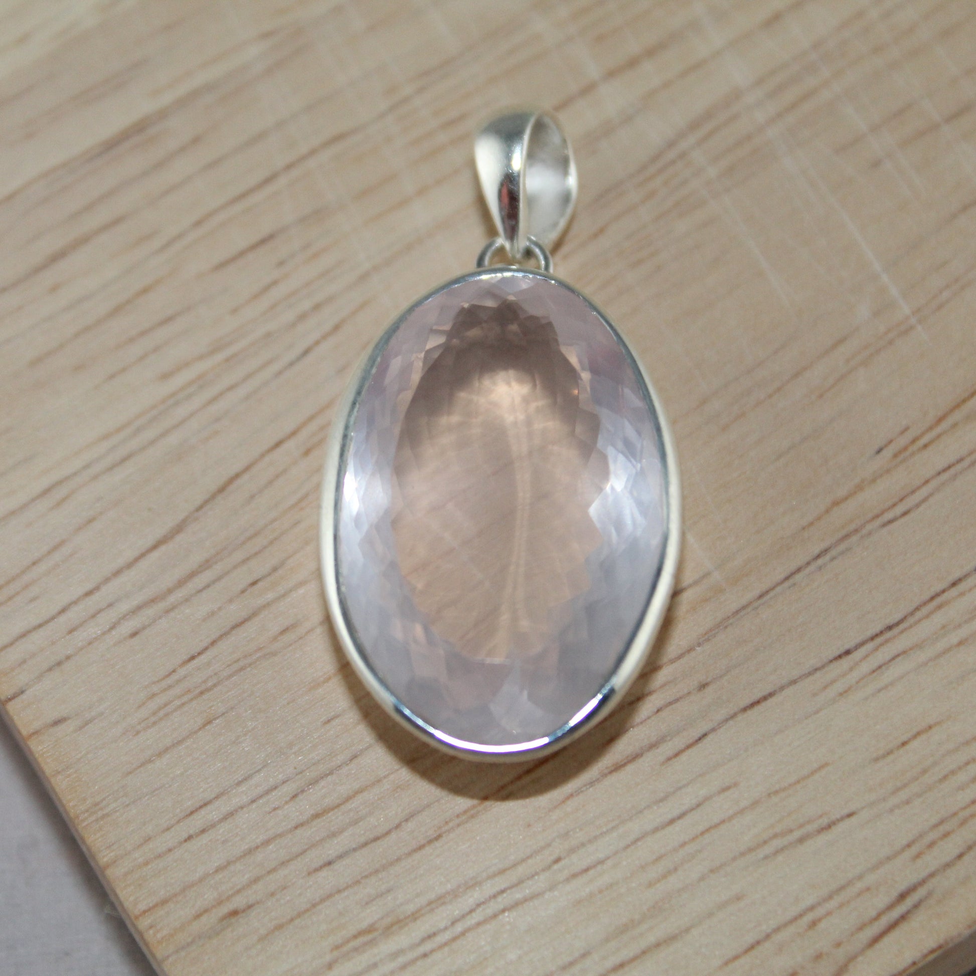 Silver pendant with a rose quartz stone on a wooden surface