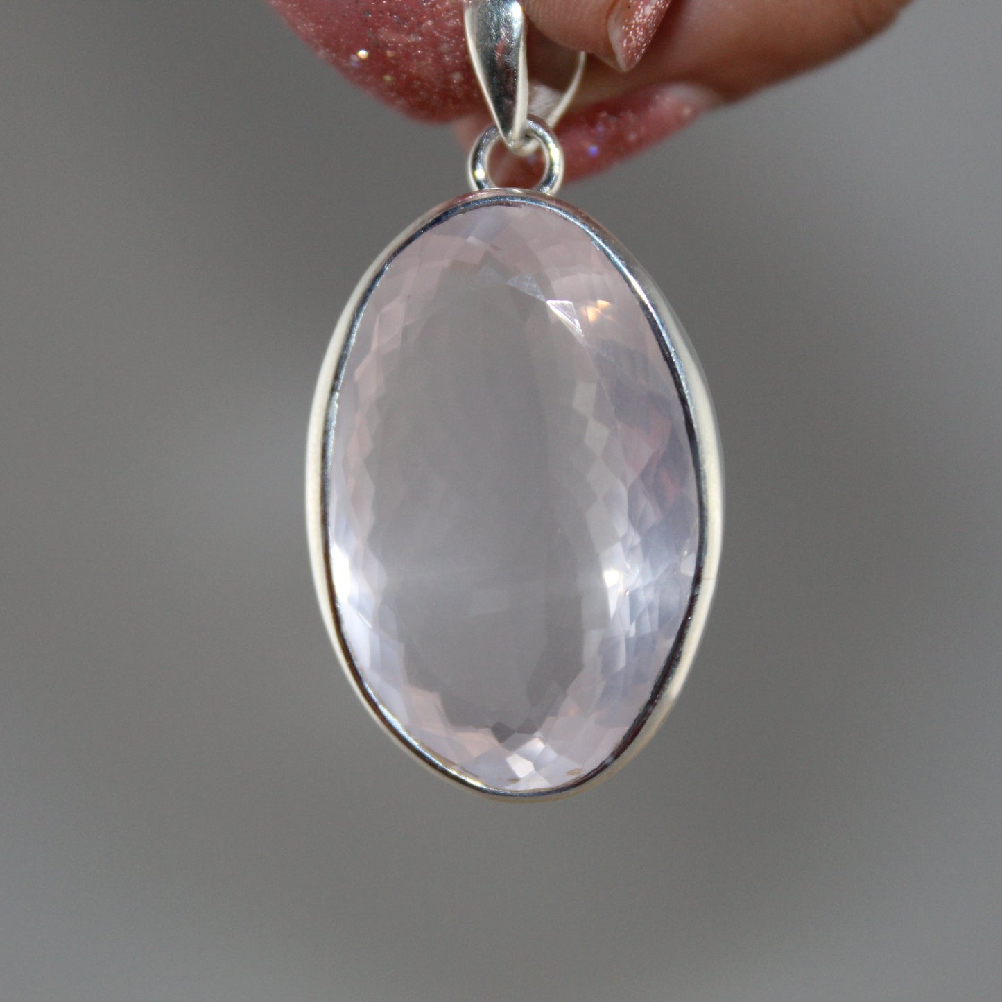 Rose quartz pendant on silver chain held by a hand against a neutral background