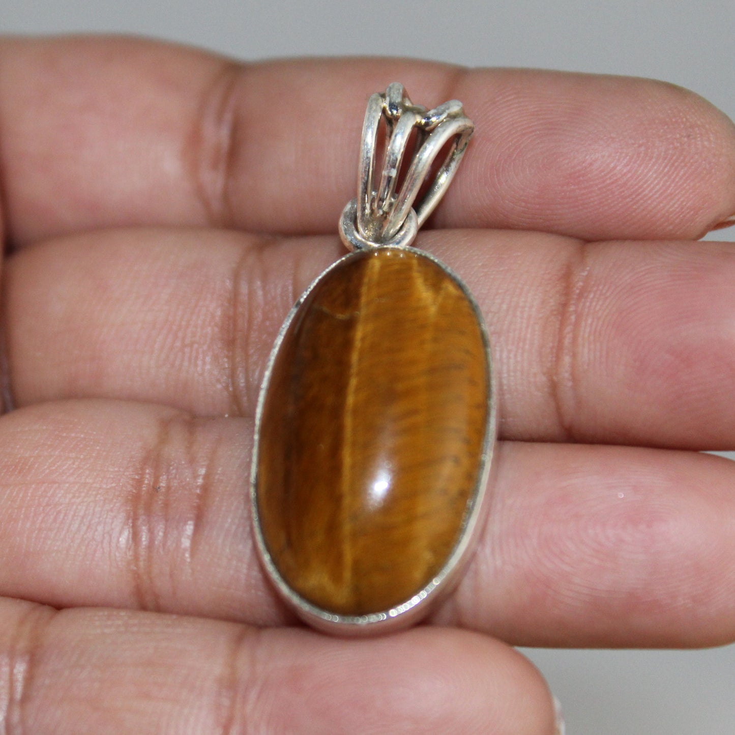 Tiger's eye pendant on a hand with a neutral background