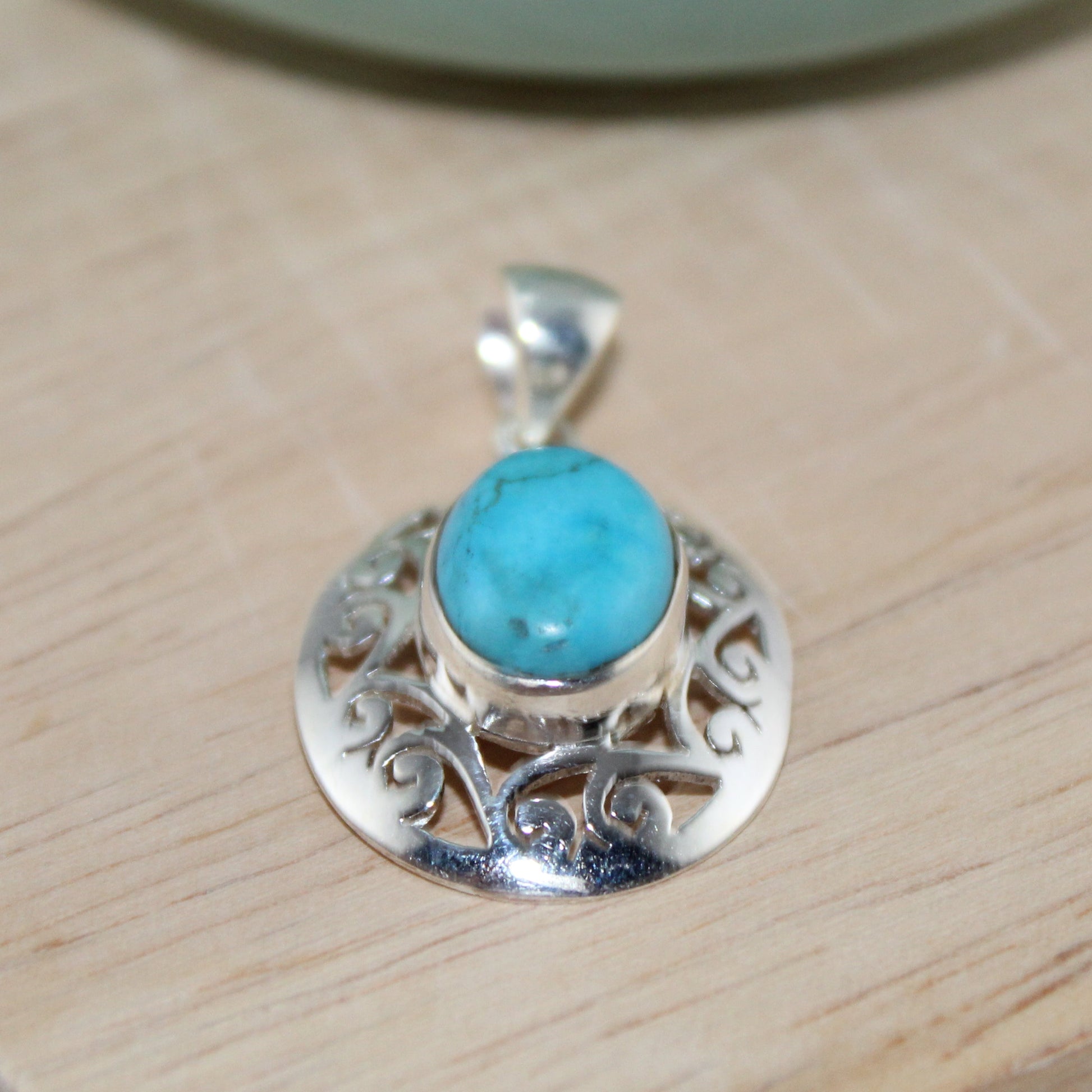 Silver pendant with a turquoise stone on a wooden surface