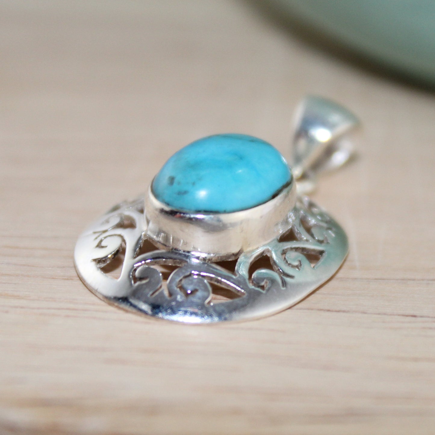 Silver pendant with turquoise stone on a wooden surface