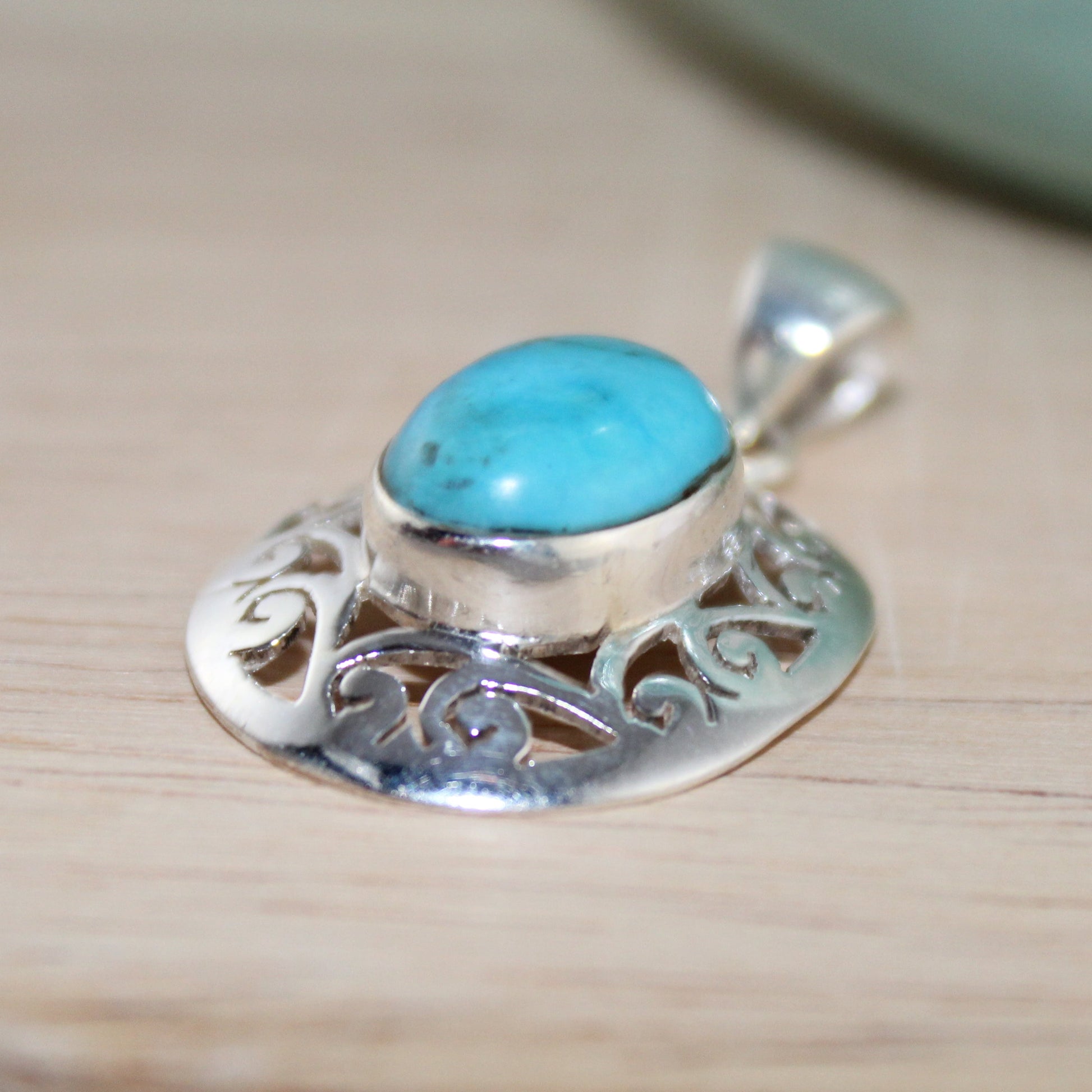 Silver pendant with turquoise stone on a wooden surface