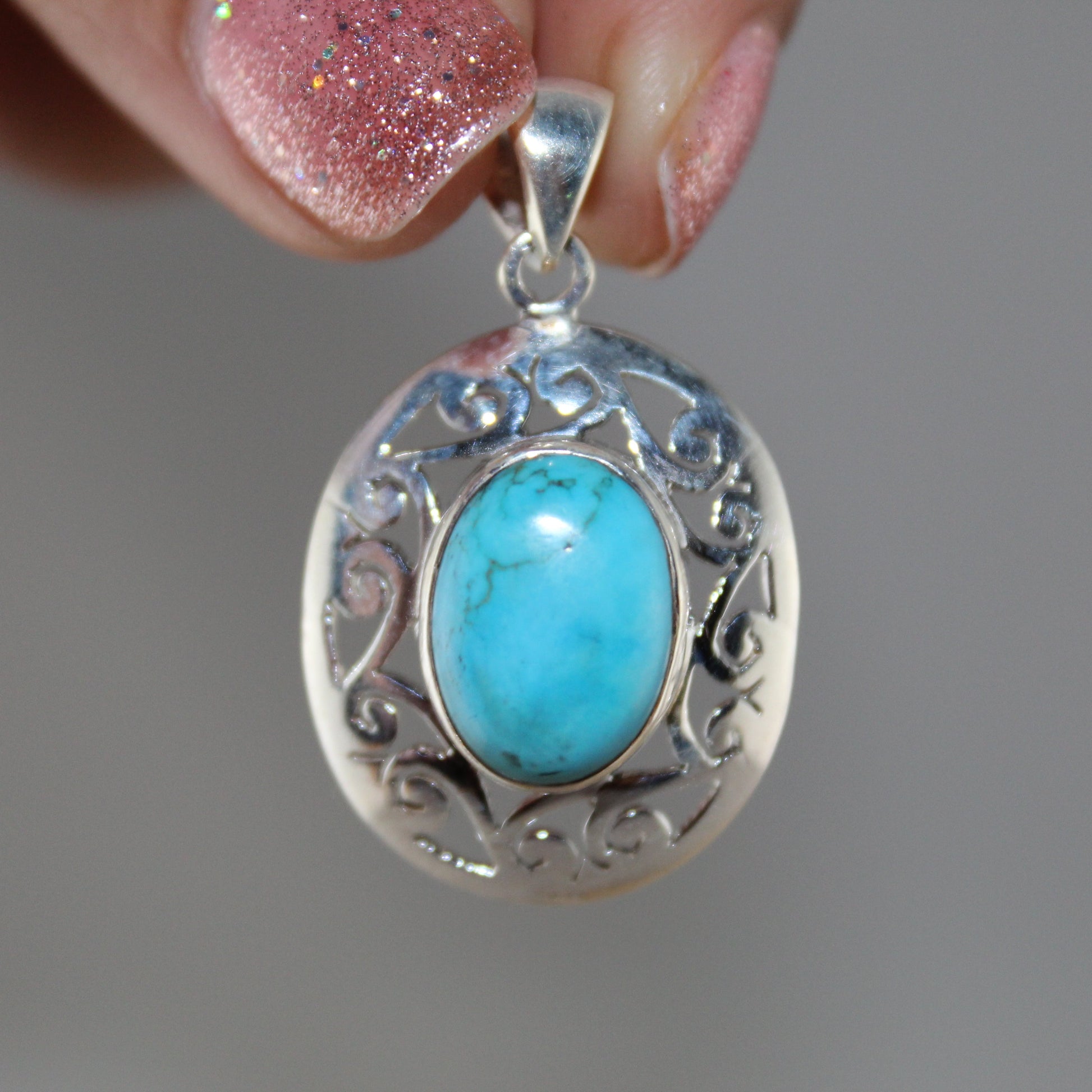 Turquoise stone pendant with silver frame held by a hand against a gray background