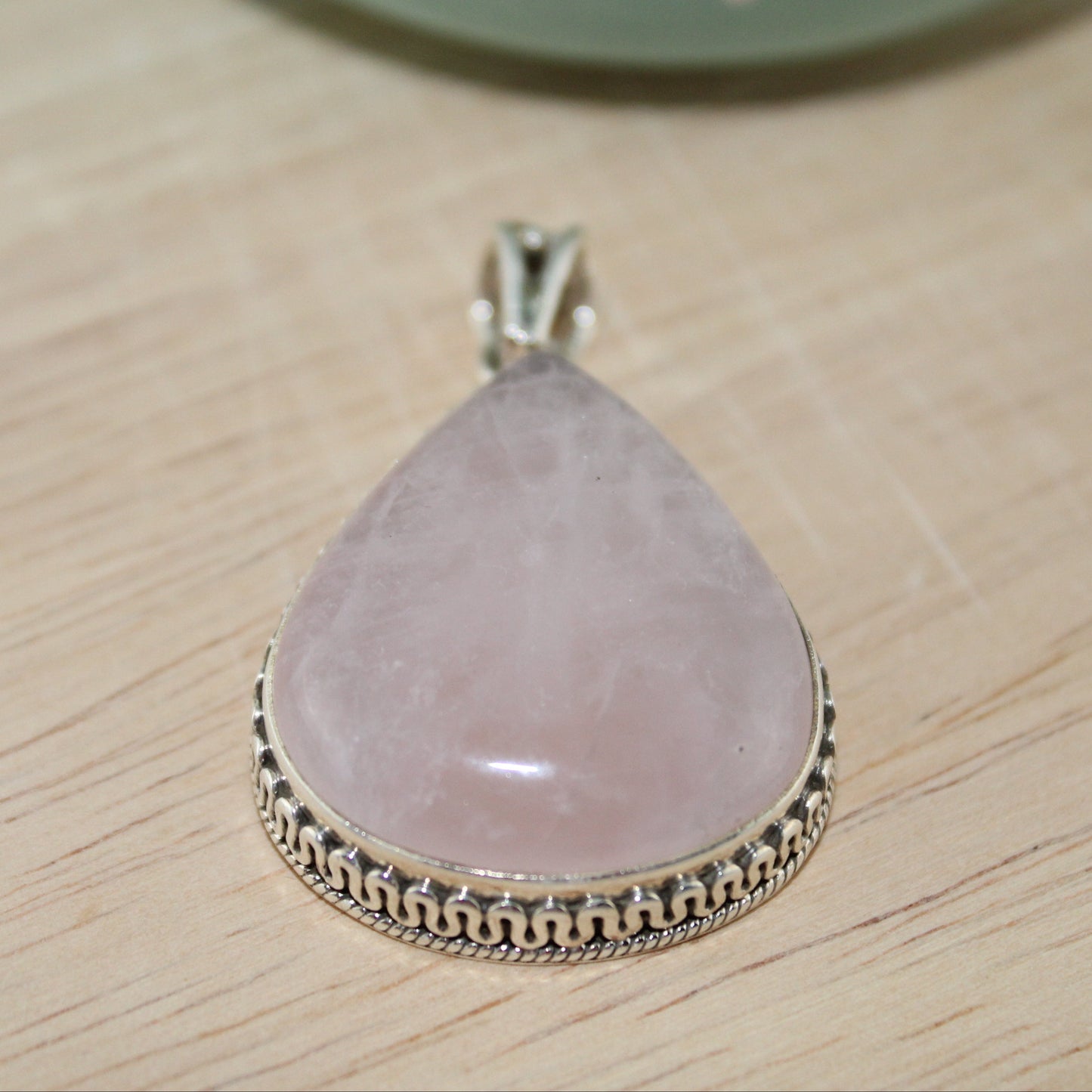 Pink teardrop pendant with silver border on a wooden surface
