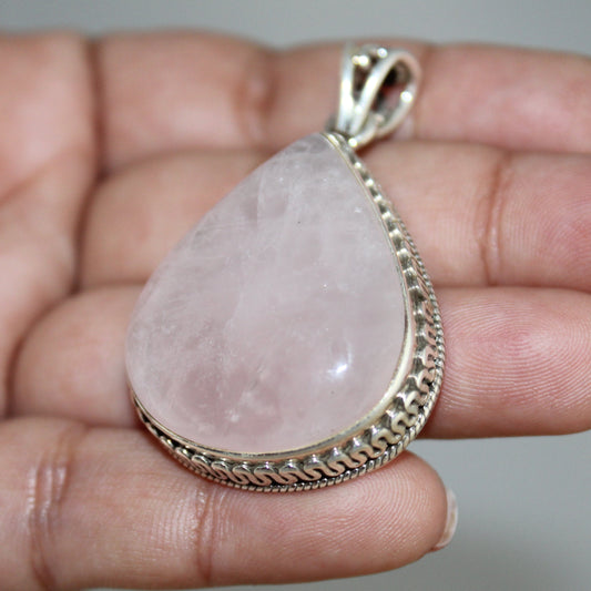 Rose quartz pendant with silver frame held in a hand against a neutral background
