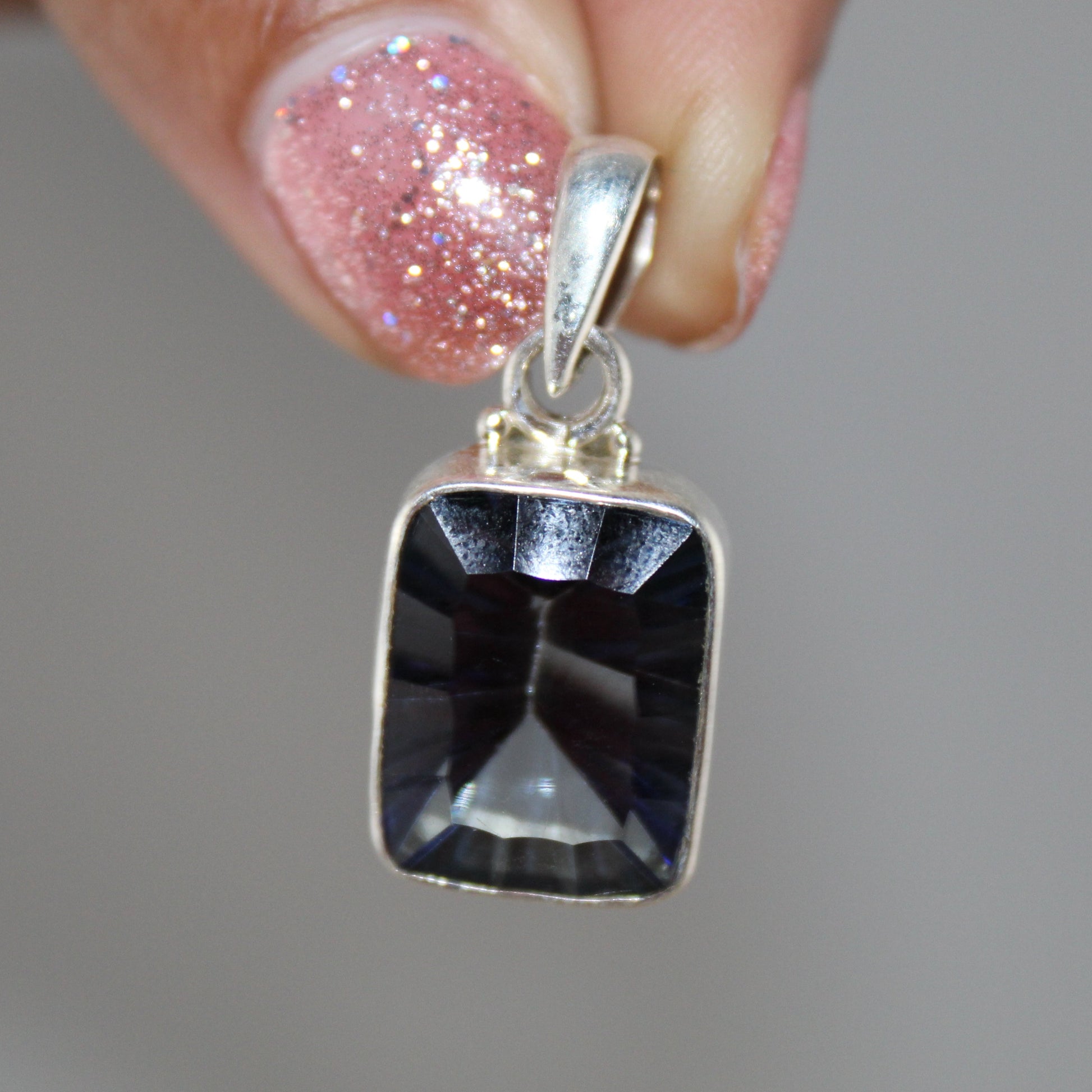Silver pendant with a black stone held by a hand against a gray background