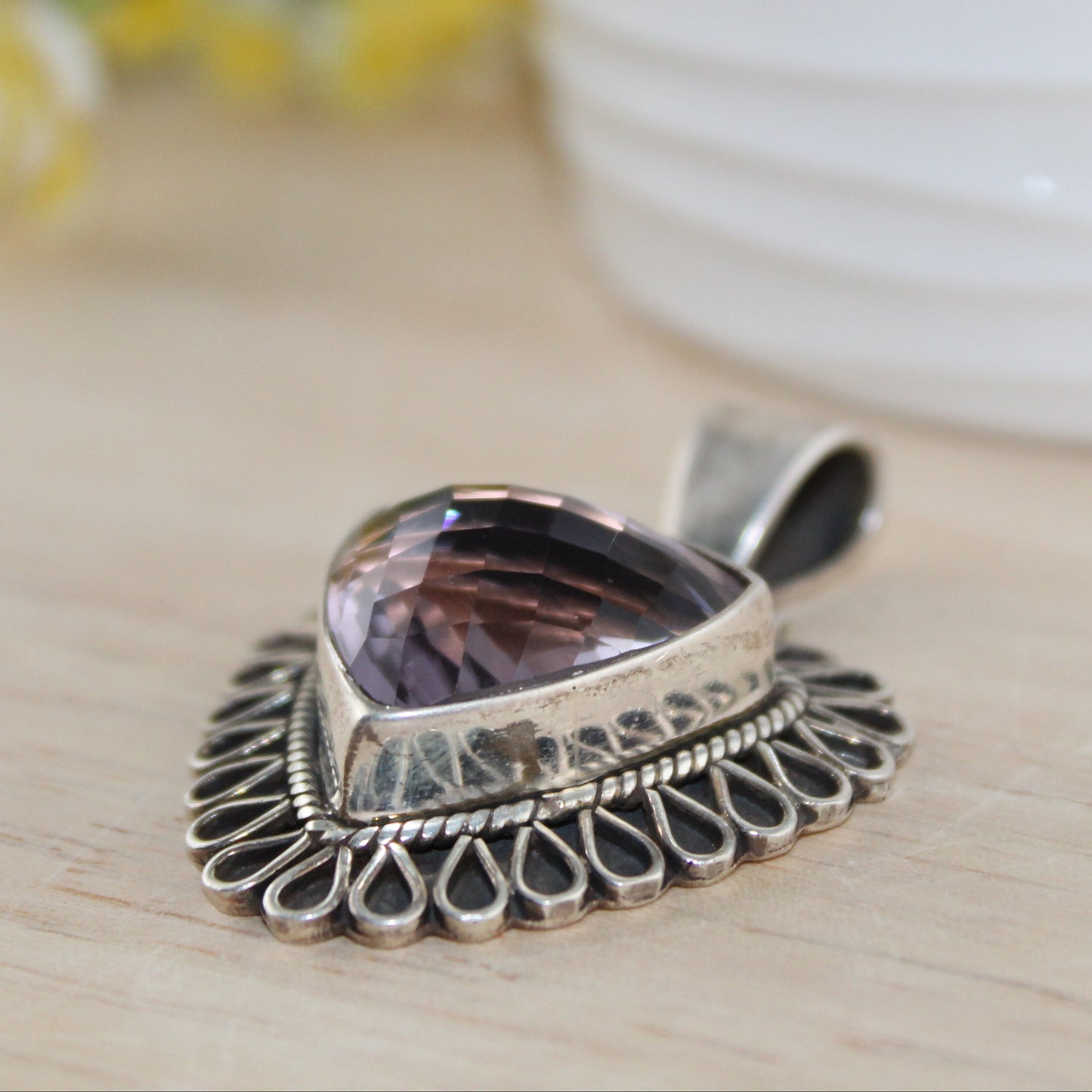 Silver pendant with a purple stone on a wooden surface with flowers in the background