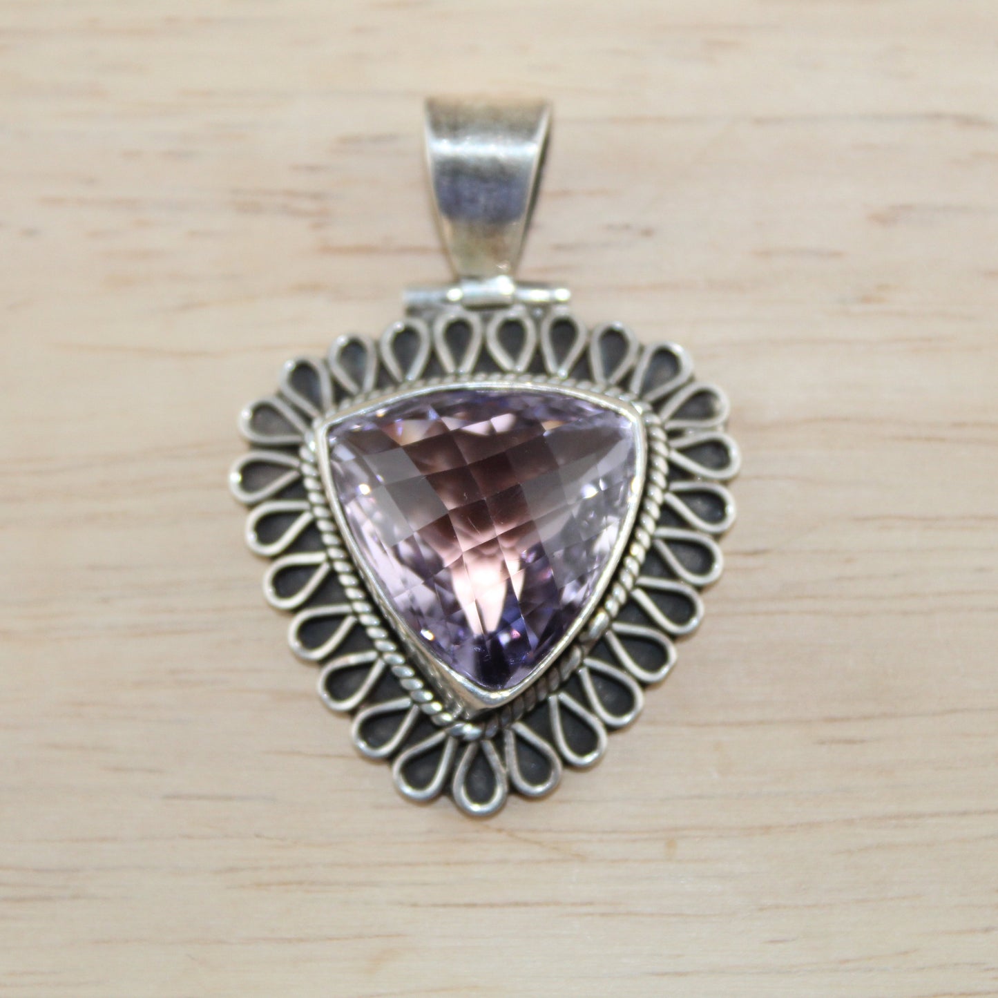Silver pendant with a purple gemstone on a wooden surface
